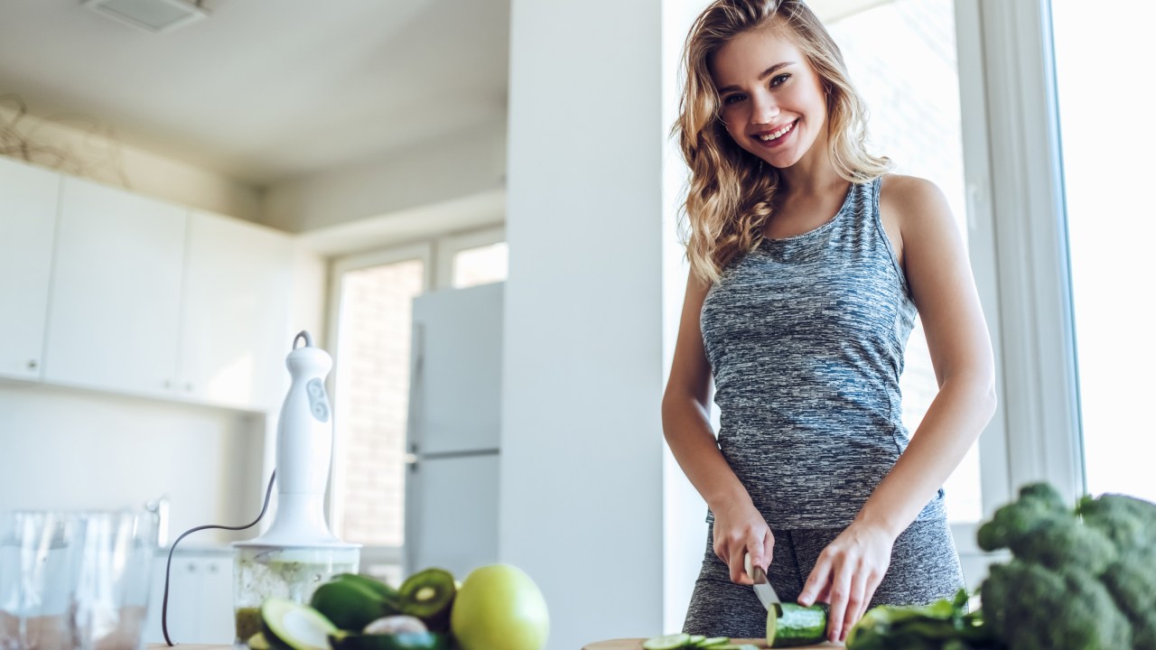 Mulher com roupas esportivas cortando alimentos saudáveis