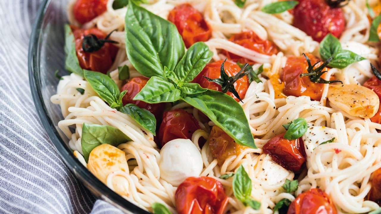 Uma vasilha de macarrão caprese servida com queijo, tomate e manjericão.