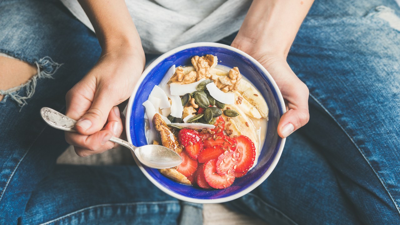 Mulher comendo iogurte com frutas e sementes em um bowl