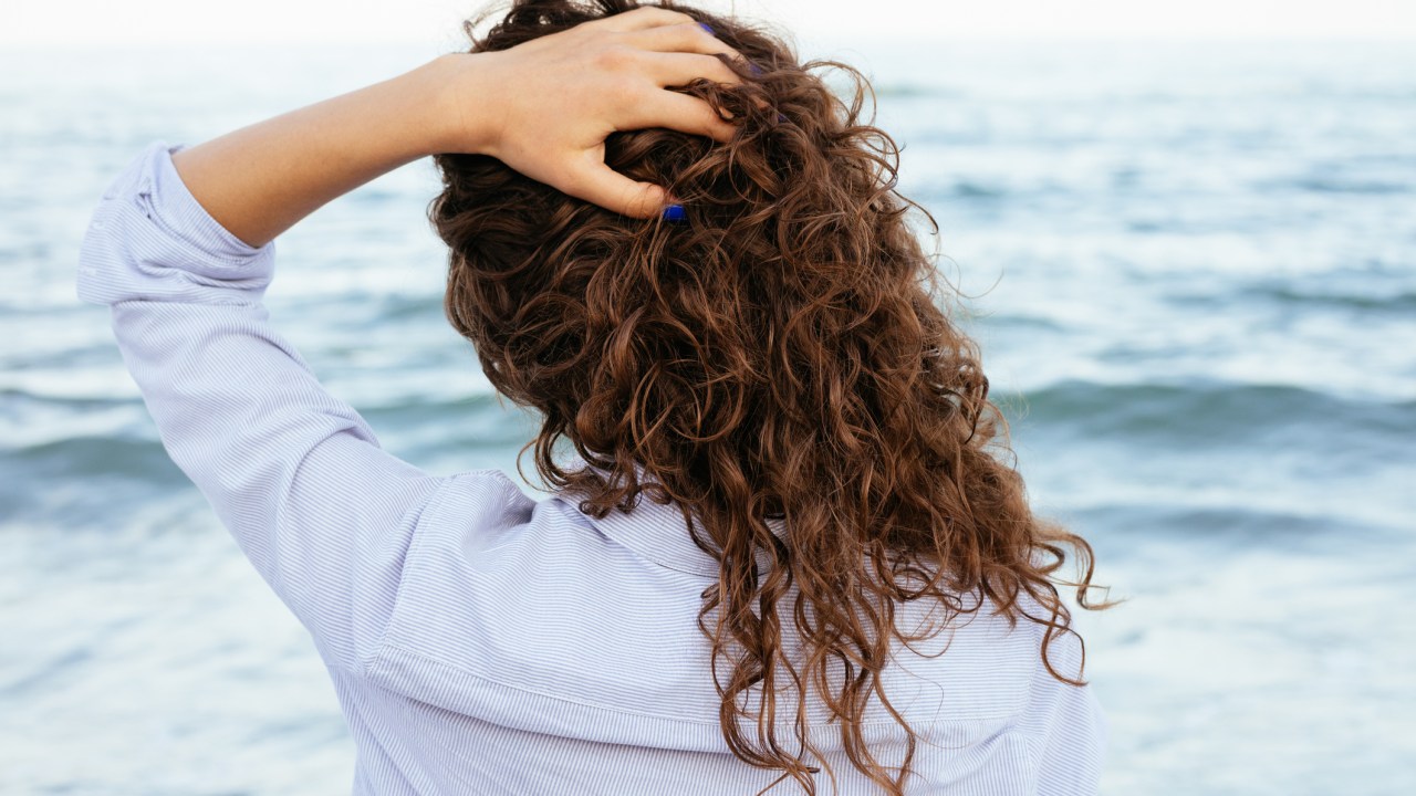 Mulher de costas com cabelo cacheado e mão na cabeça