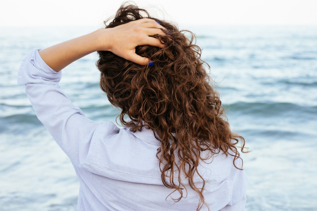 Mulher de costas com cabelo cacheado e mão na cabeça