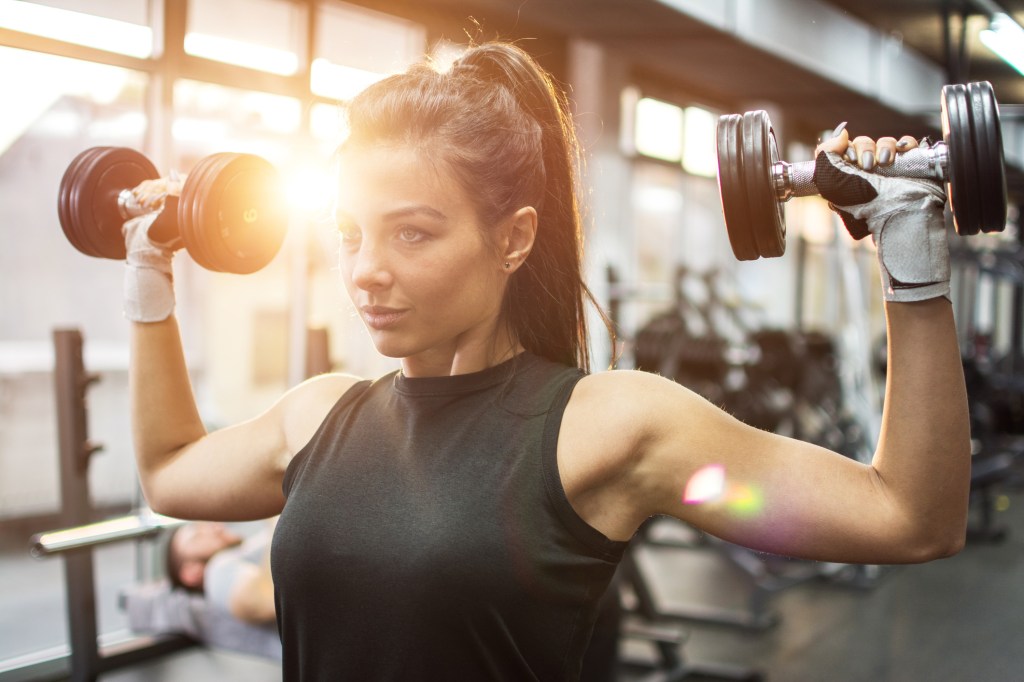 Mulher na academia segurando dois halteres