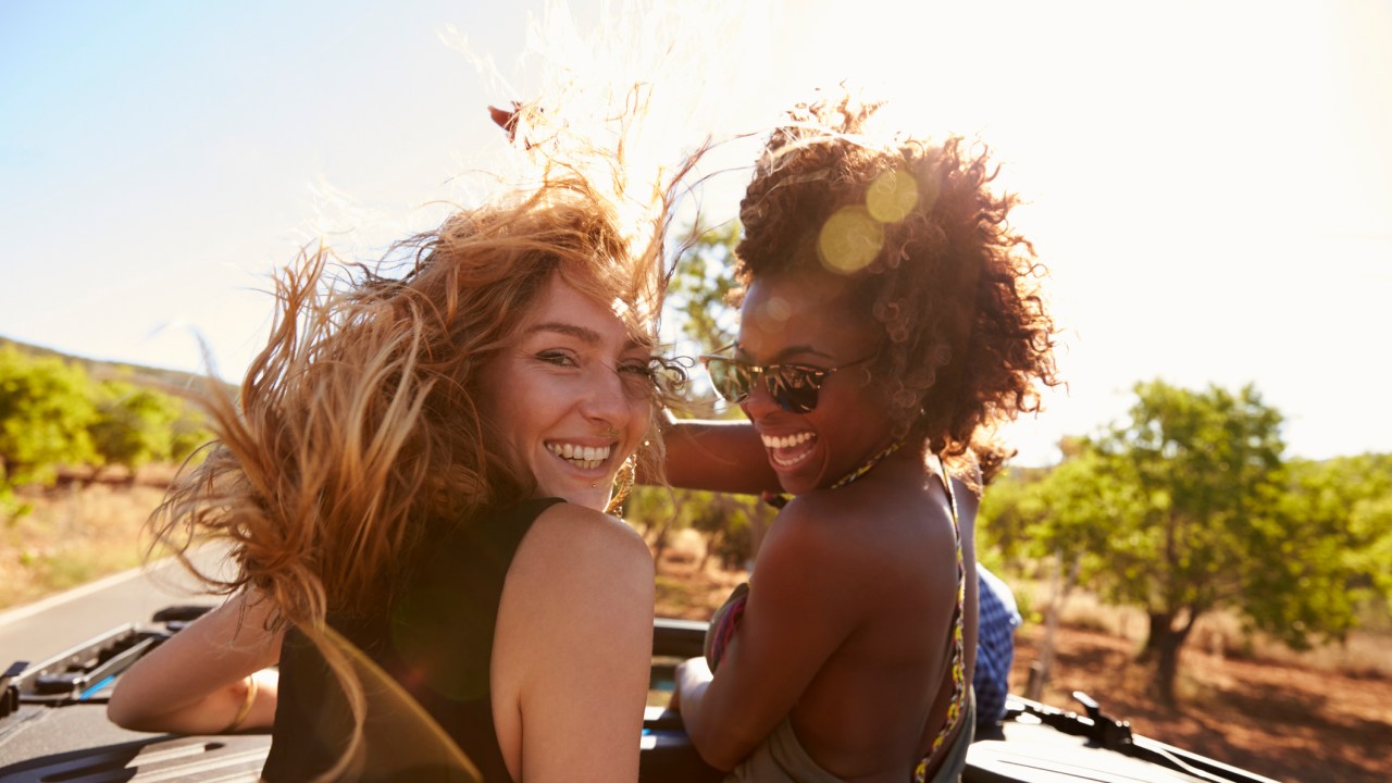 Duas amigas andando de carro conversível com o cabelo ao vento