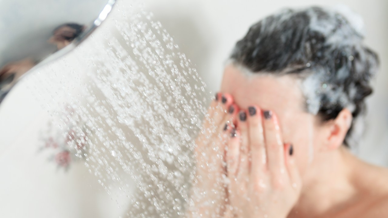 Mulher tomando banho de chuveiro com a mão no rosto