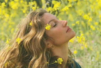 Mulher sentada no jardim de olhos fechados, sentindo o sol na pele e flores nos cabelos