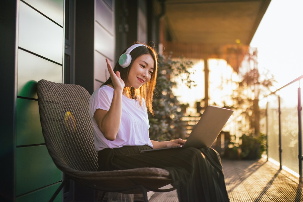 Confident Young Woman With Headphones Having A Conference Call On Laptop At The Balcony Como fazer amizades