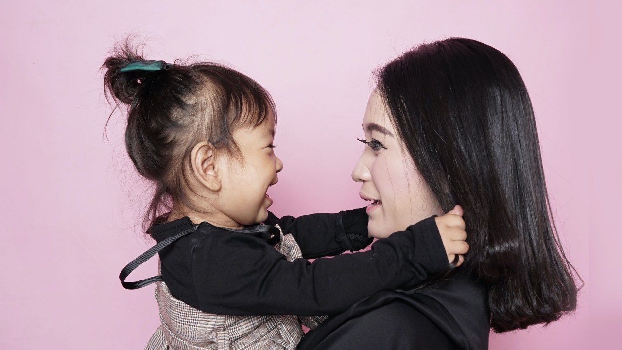 Mãe e filha pequena se abraçando em fundo rosa