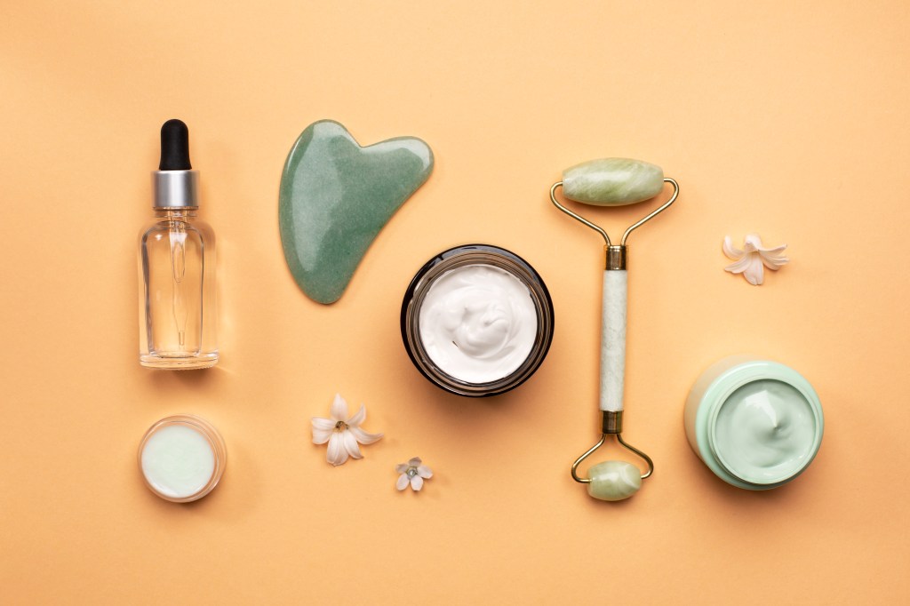 produtos de skincare como gua sha, sérum, creme, esfoliante, jade roller posicionados deitados em fundo laranja