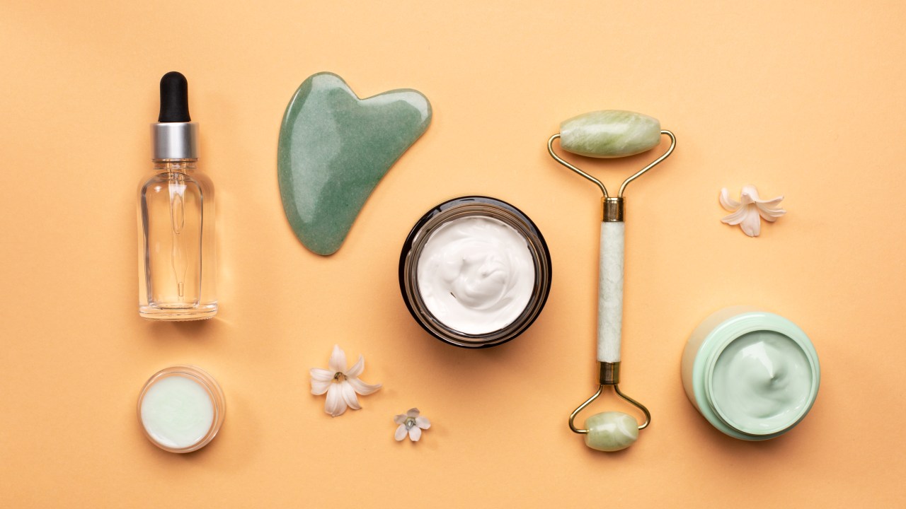 produtos de skincare como gua sha, sérum, creme, esfoliante, jade roller posicionados deitados em fundo laranja