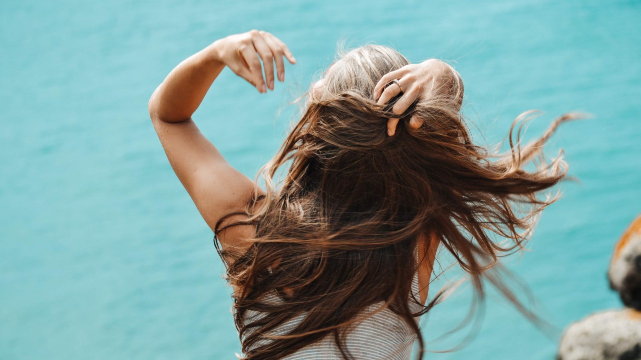 mulher de costas, arrumando o cabelo longo e escuro