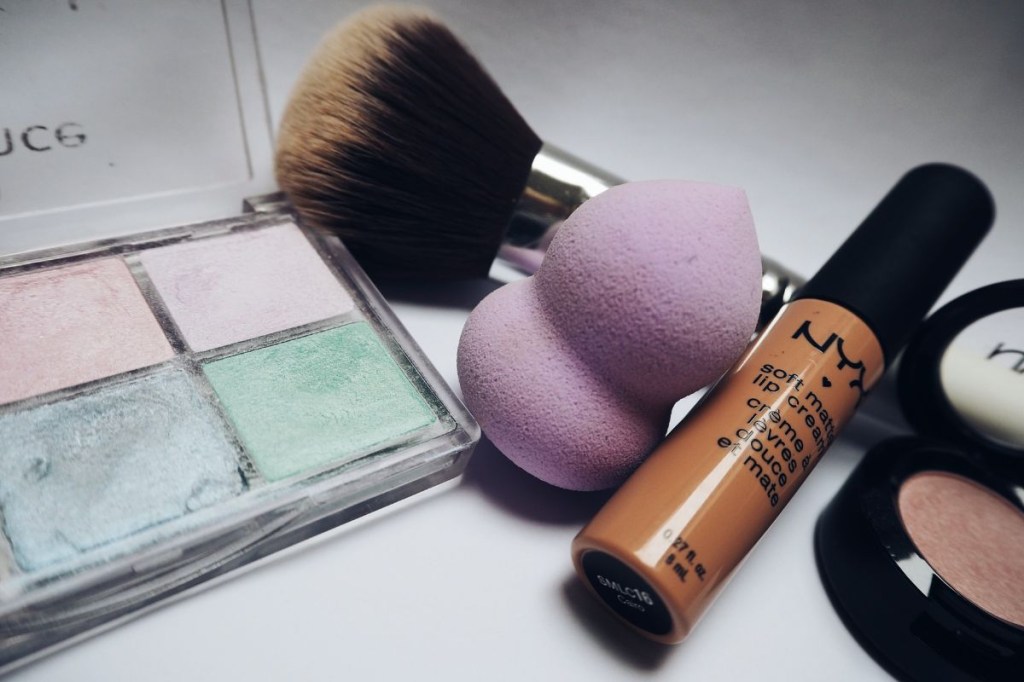 Paleta de sombras com corretivo da marca Nyx e pincel de maquiagem ao lado