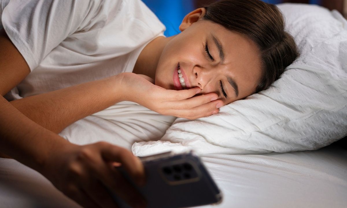 Pessoa deitada na cama mexendo no celular